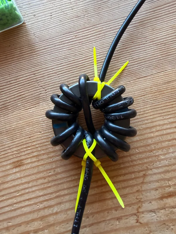 Coaxial cable wound through a ferrite ring and held with zip ties, a choke that keeps unwanted current off an antenna feed line.