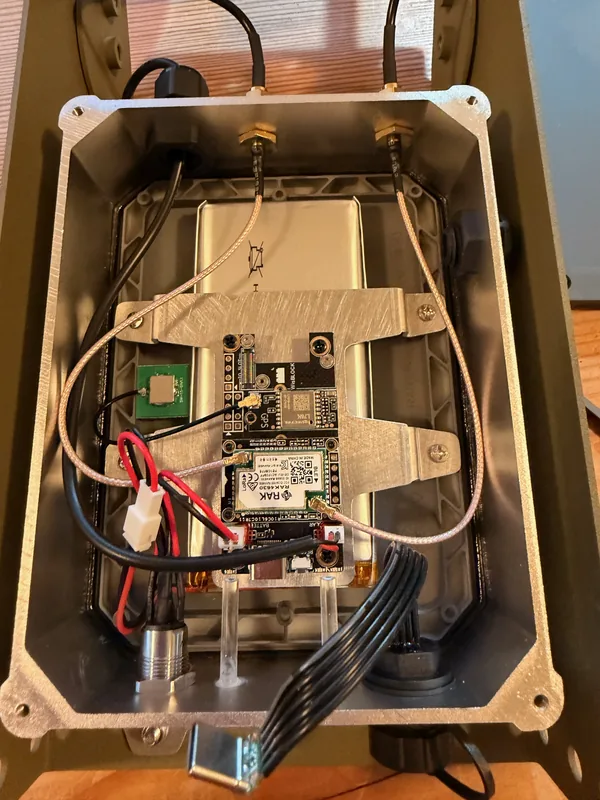 A LoRa mesh radio built into a weatherproof enclosure, with its circuit board, battery pack, and antenna cables.